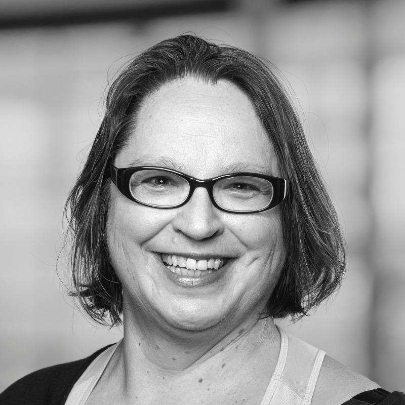 Portraitfoto in schwarz weiß. Lachende Frau mit Brille und halblangen dunklen Haaren. Abgebildet ist Sibylle Kraus die Künstlerin.